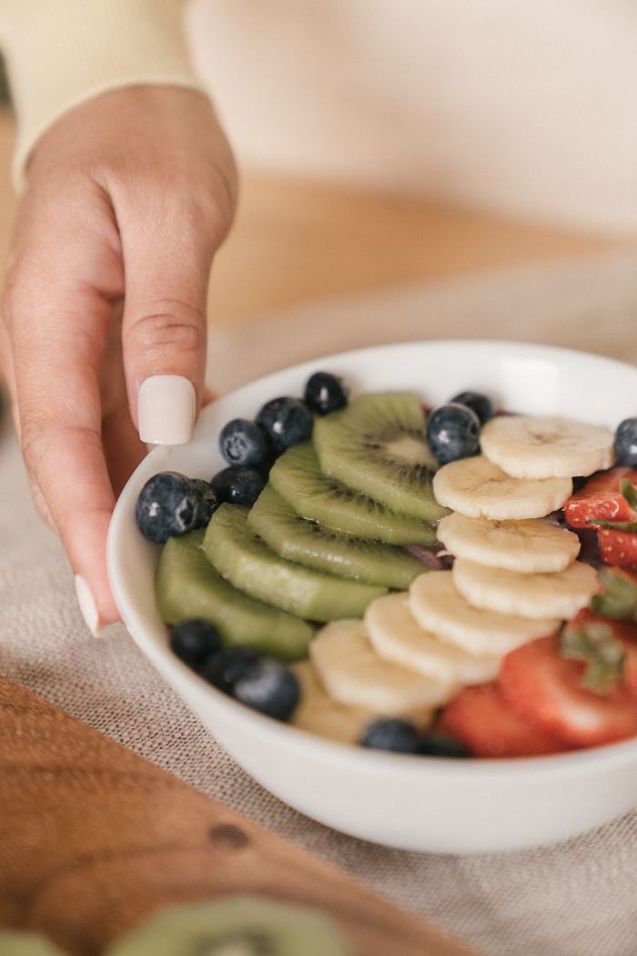 services-04 A ceramic bowl filled with fresh sliced kiwi, banana, blueberries, and strawberries, ideal for healthy eating.